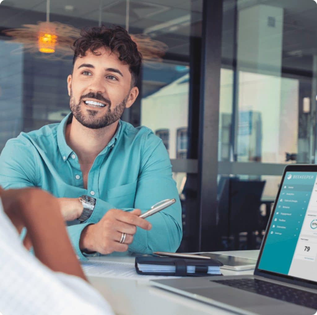 Smiling man pointing at computer screen as if discussing something on screen with the viewer